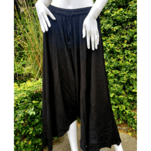 A woman standing in front of bushes wearing black pants.