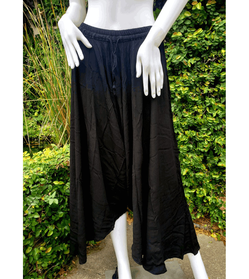 A woman standing in front of bushes wearing black pants.