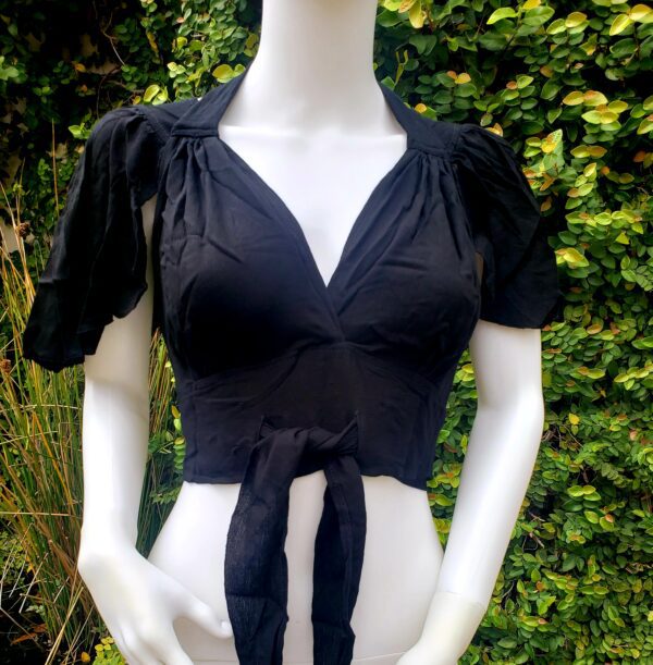 A mannequin wearing black clothing with bushes in the background.