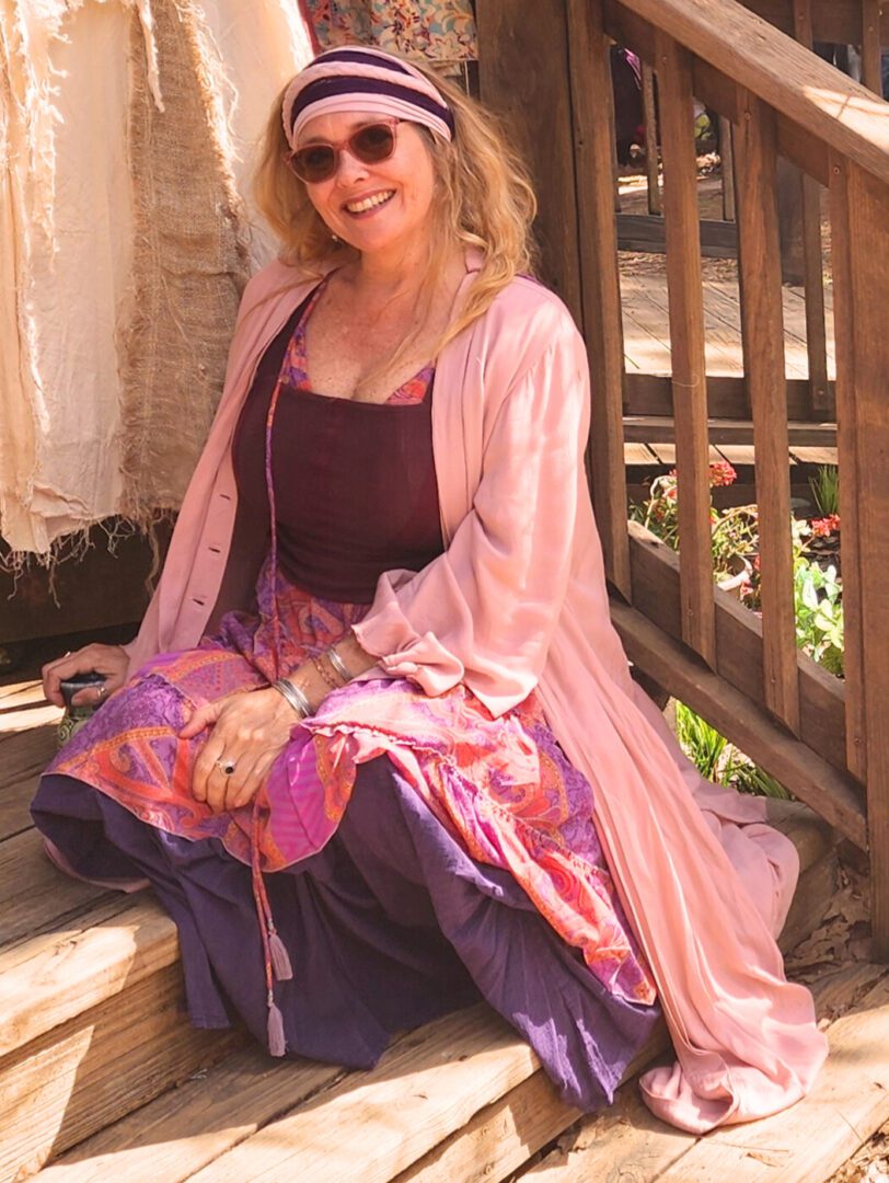 Woman in colorful bohemian attire sitting outdoors.